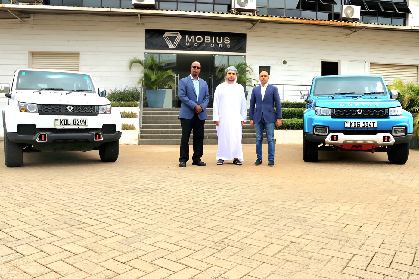 Three men stand between two Mobius vehicles outside the company’s premises.